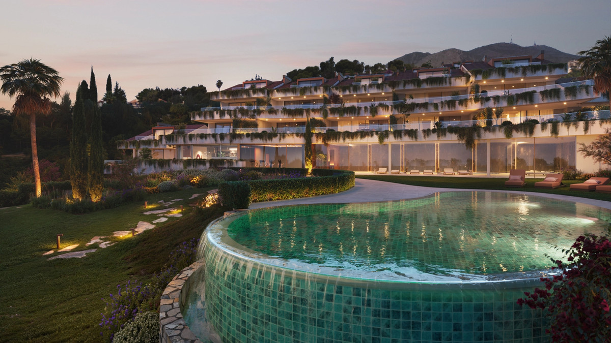 Casatalaya Residences – Benalmadena - illuminated exterior facade with terraced balconies, lush gardens and circular mosaic pool at dusk