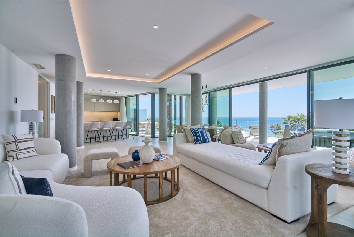 The Sapphire – Estepona - spacious open-plan living room with white sofas, concrete columns, and panoramic sea views through floor-to-ceiling glass