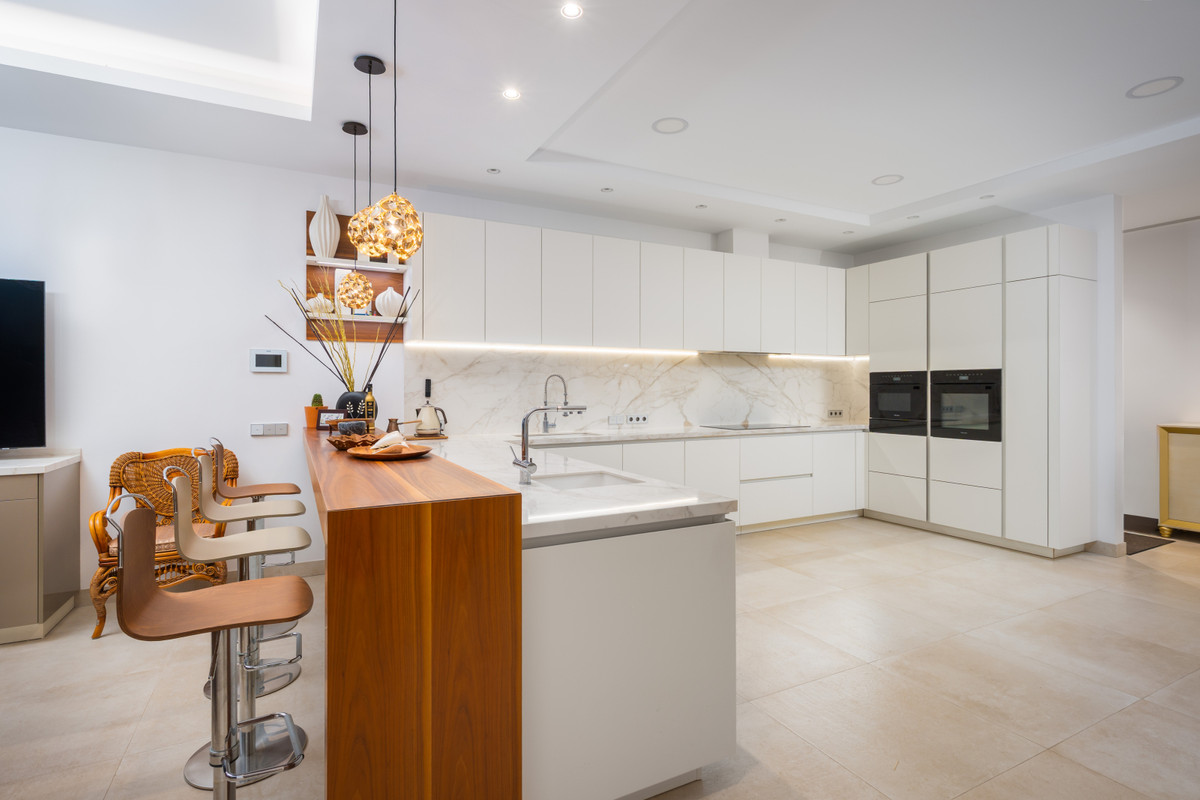 Villa Murcia – Estepona - sleek open-plan kitchen with white cabinetry, marble backsplash, and wooden island breakfast bar