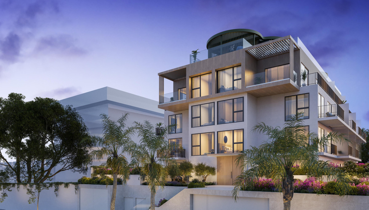 Ykines – Torremolinos - modern luxury apartment building exterior at dusk with illuminated balconies and rooftop terrace surrounded by palm trees